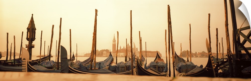 A line of gondola boats are photographed in panoramic view as they sit docked in the water.