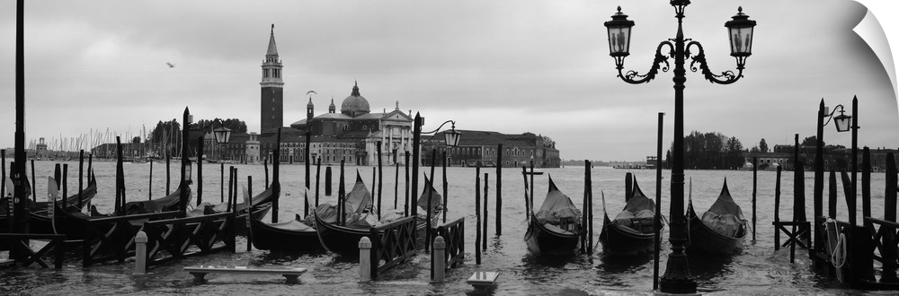 Wide angle photograph of a line of gondolas parked near the shore, the Church Of San Giorgio Maggiore on the distant horiz...