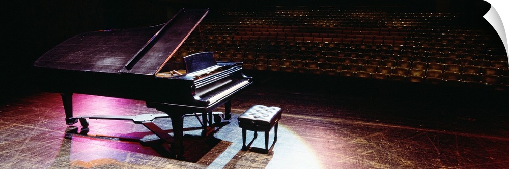 Full grand piano on a well-worn stage in a theater, looking out onto the rows of empty seats, under violet spotlights.
