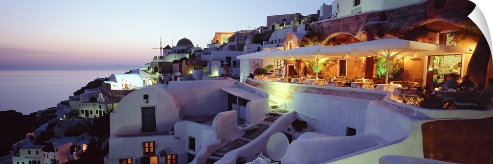 Beautiful white faoade buildings sit on a hill overlooking the Mediterranean Ocean in Santorini, Greece as the pastel sky ...