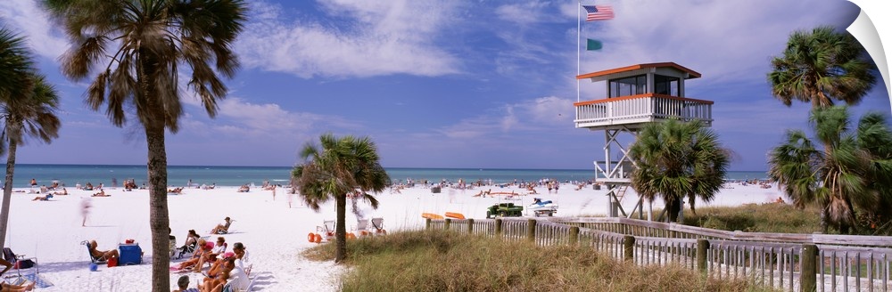 Panoramic print of a crowded beach with a lifeguard stand and palm trees.