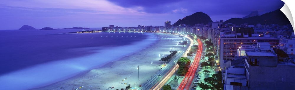 Grand panoramic of Copacabana Beach in Rio de Janeiro at dusk as the cars go speeding by on the beach front road.