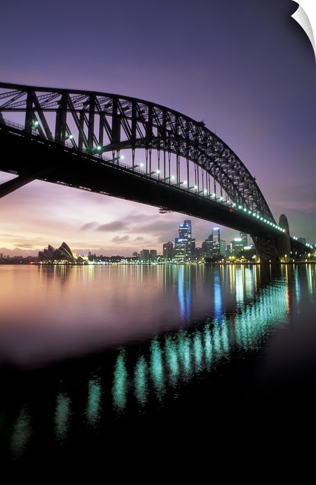 Steel arch bridge crossing over the harbor in the evening, with the Sydney Opera house in the distance.