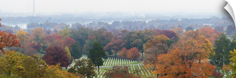 An ariel photograph of Arlington National Cemetery surrounded by autumn colored trees and a view of the Washington monumen...
