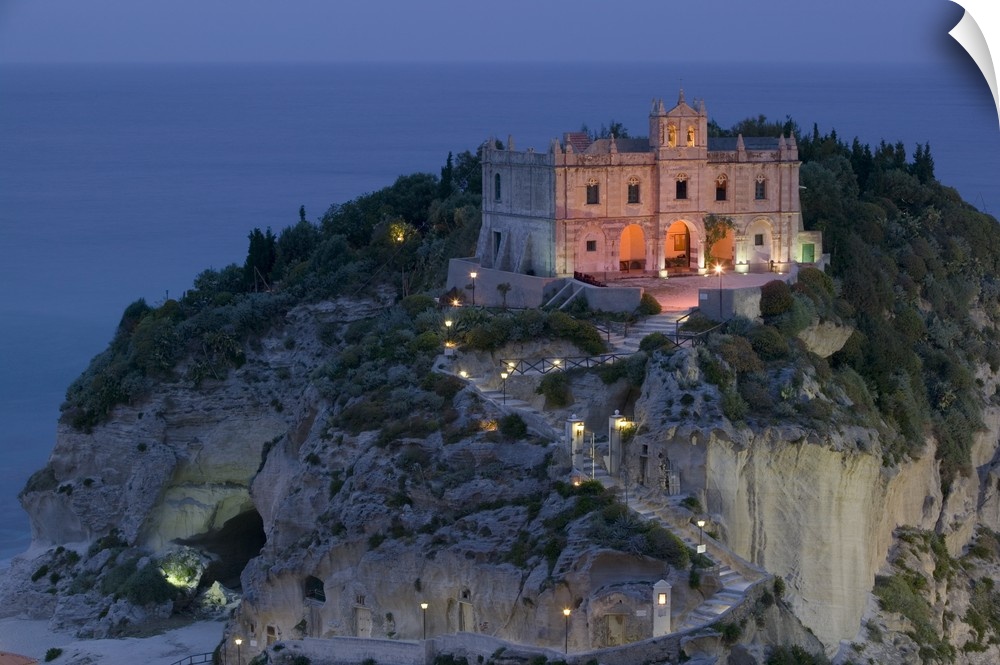 A large church sits on a huge cliff and is illuminated under an evening sky.