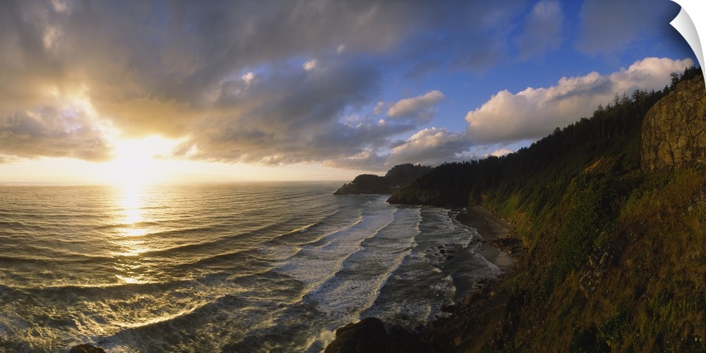 Photograph of steep shoreline with waves rolling in under a bright cloudy sky at sunrise.