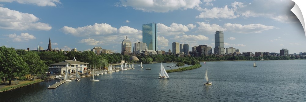 A panoramic photograph of Charles river with sail boats and the Boston skyline in the background. Trees line the edge of t...