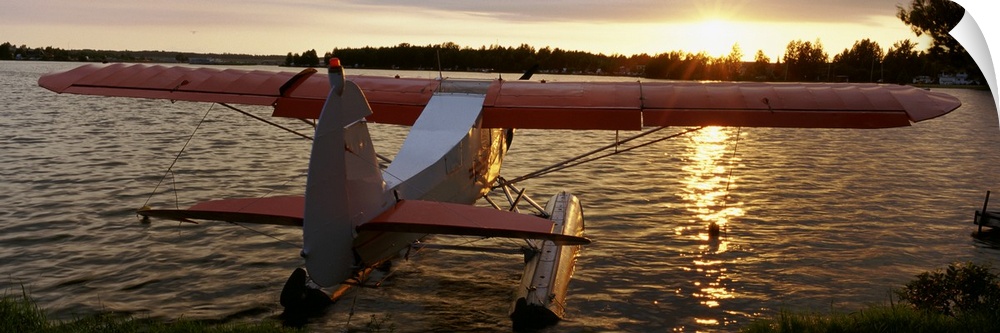 Panoramic photograph of plane sitting in water with forest in the distance at sunset.
