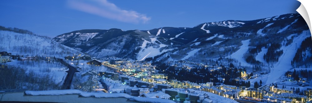 Panoramic photograph of a  snowy mountain landscape surrounding the brightly lit town of Telluride, Colorado at night.