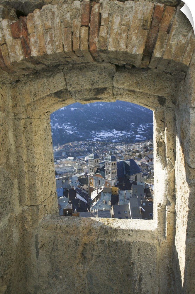 A photograph is taken through a small stone edged window of a town below.