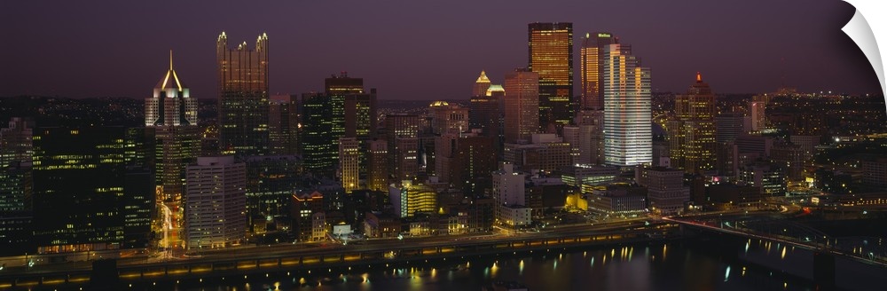 Panoramic photograph of skyline at dusk with tall buildings and skyscrapers glowing in the dark sky.