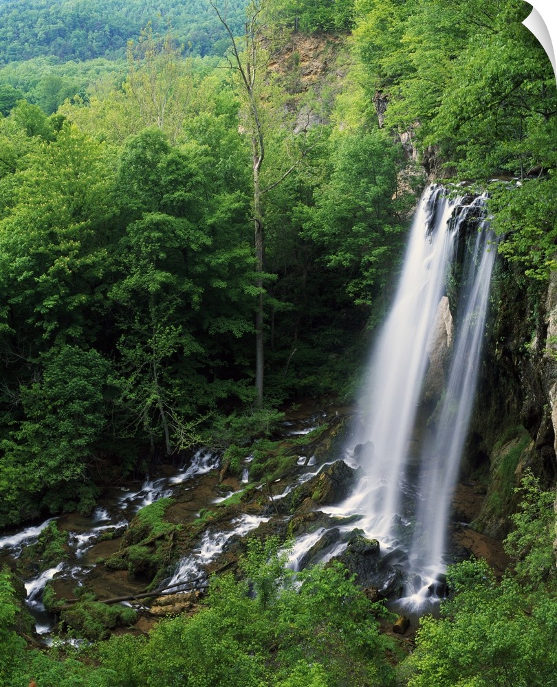 A large waterfall is photographed from above as it falls onto rocks and is surrounded by thick forest.