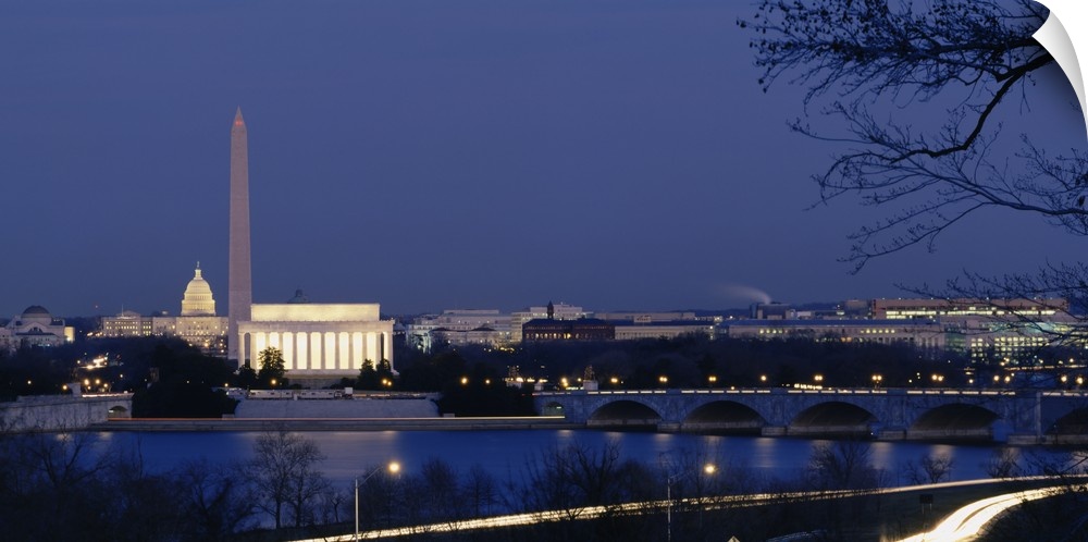 Wall art of major illuminated DC landmarks layered in the distance of a waterfront that a bridge passes over at dusk.