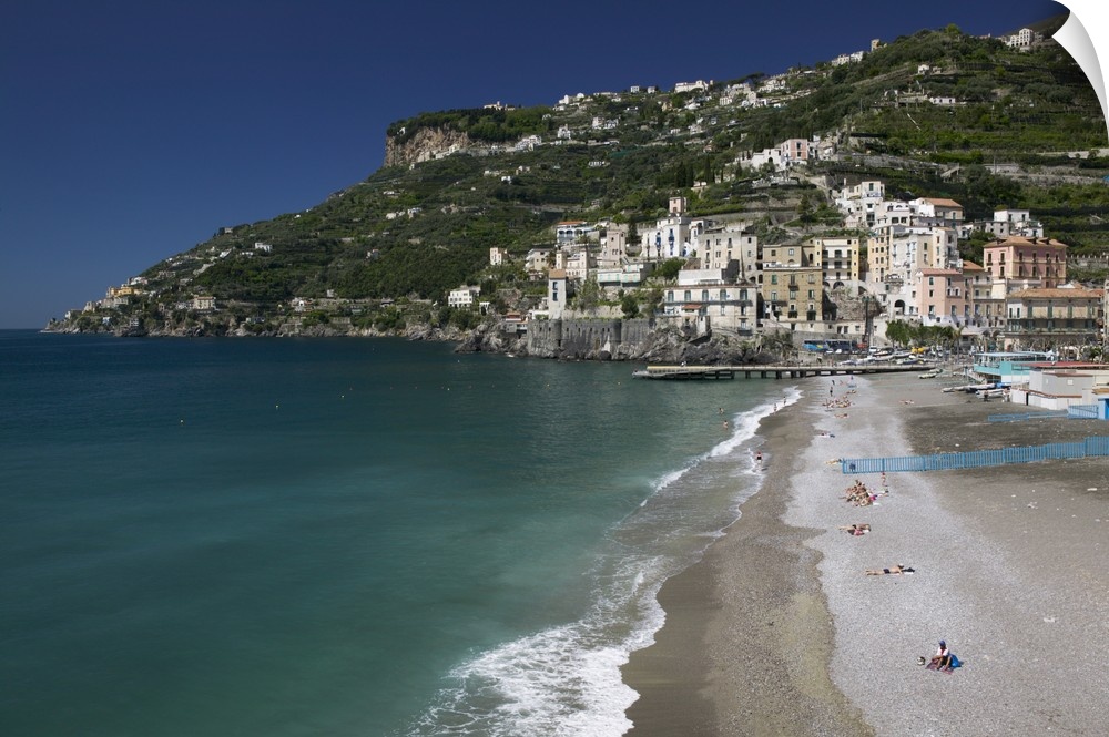 A large cliff with buildings and homes built in it is photographed with the ocean water and beach in view.
