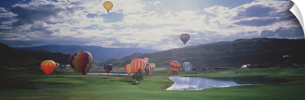 This is a landscape photograph of hot air balloons lifting off from a field on the valley floor in the mountains.