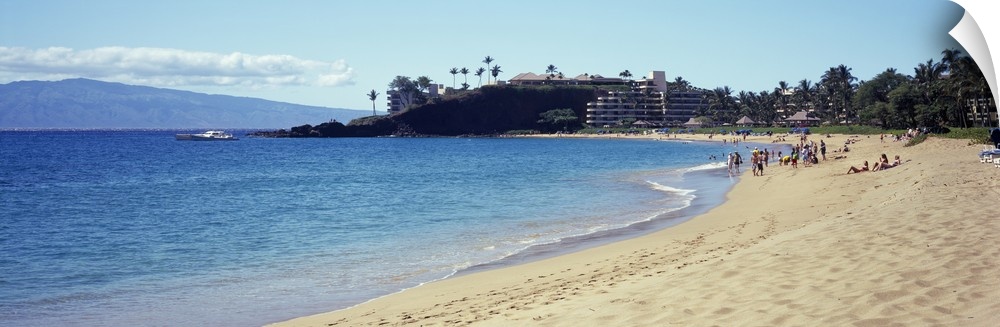 Wide angle photograph taken of a Hawaiian coast with people on the beach and a hotel in the distance.
