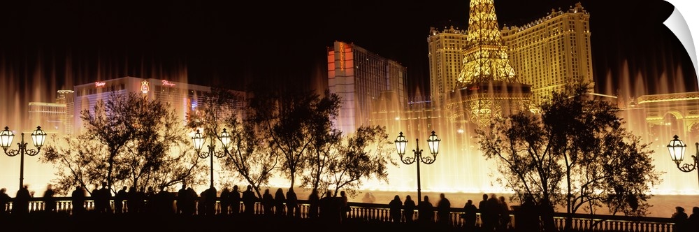 Large panoramic photograph of the Las Vegas strip lit up with the silhouette of people and trees in the foreground.