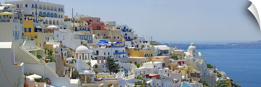 Houses in Greece are photographed from the side as they sit high up in a large cliff off the coast.