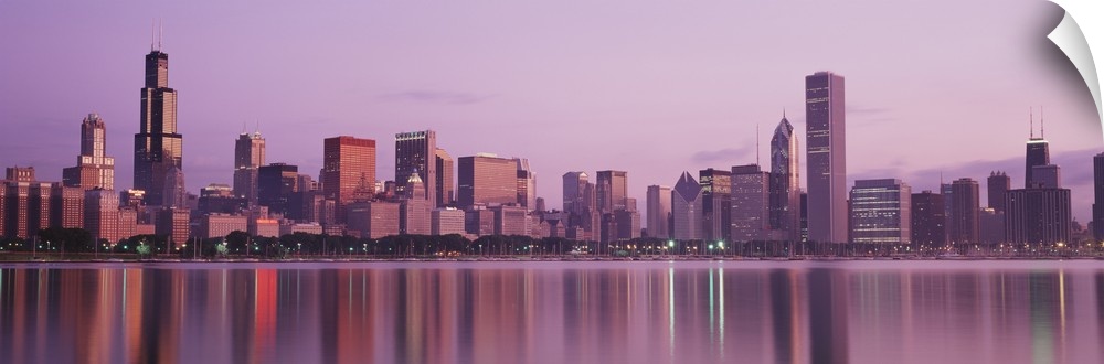 Panoramic photograph of skyline and waterfront lit up at dusk.  The buildings are reflected in the water below.