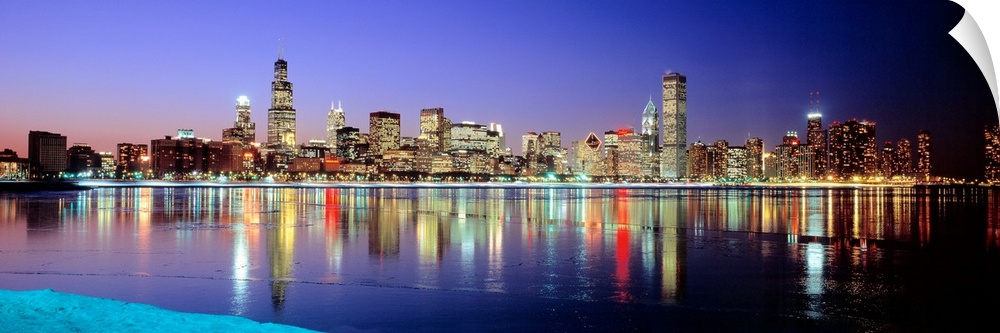 Panoramic photographic canvas of a cityscape illuminated with colored lights reflected perfectly onto the water at dusk.