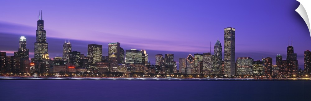 Oversized, horizontal, panoramic photograph of lit skyscrapers of the Chicago skyline at night.