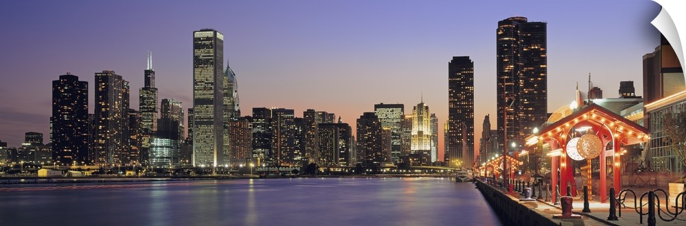 Panoramic cityscape of Chicago at the edge of Lake Michigan at dusk, with the skyscrapers lit up in the evening.