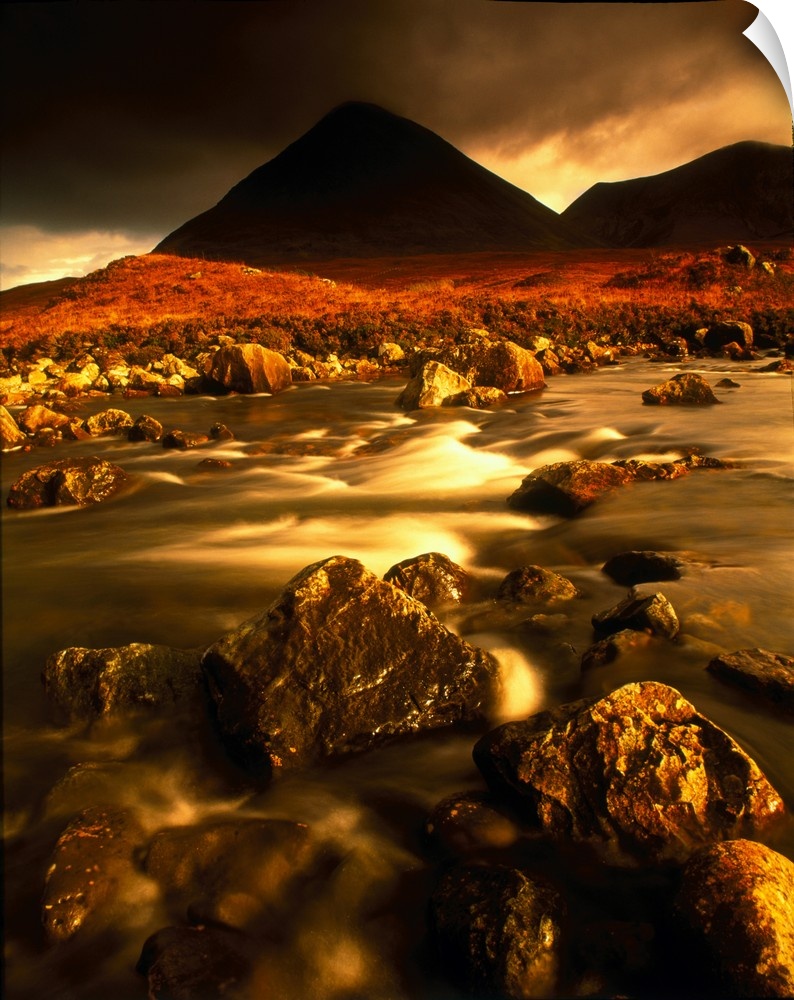 Vertical panoramic photograph of rocky river bed with mountain silhouettes in the background under a dark cloudy sky.