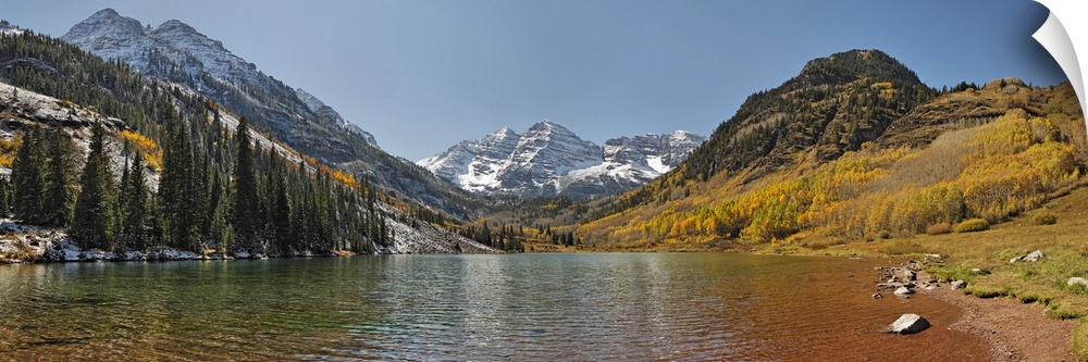 Image taken from the edge of a lake in a valley in the Rocky Mountains, surrounded by tall pine trees and snowy mountains ...
