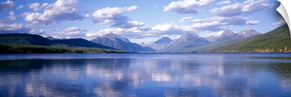 Panoramic photograph Lake McDonald with small ripples in the water reflecting the mountains and trees in the background.