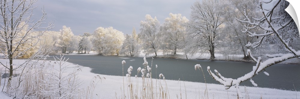 A frozen lake is photographed and surrounded by snow covered trees and land.