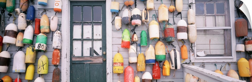Various colored and styled buoys hang on the side of a shack with a run down door in between.