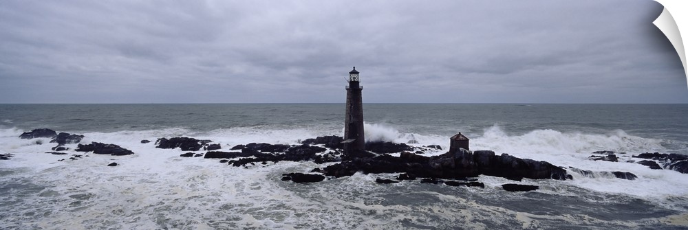 This decorative wall art is a panoramic photograph taken on an overcast day of a lighthouse built on rocks being battered ...