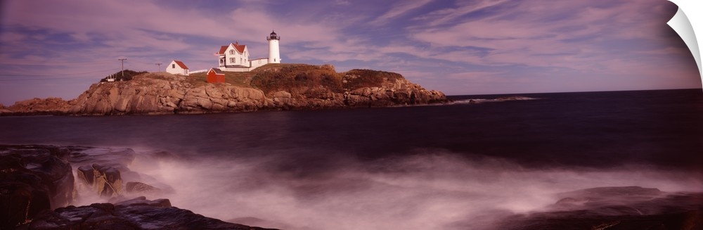 Panoramic photograph of Nubble Lighthouse on top of a rocky hillside, along the coast of York, Maine, while coastal waters...