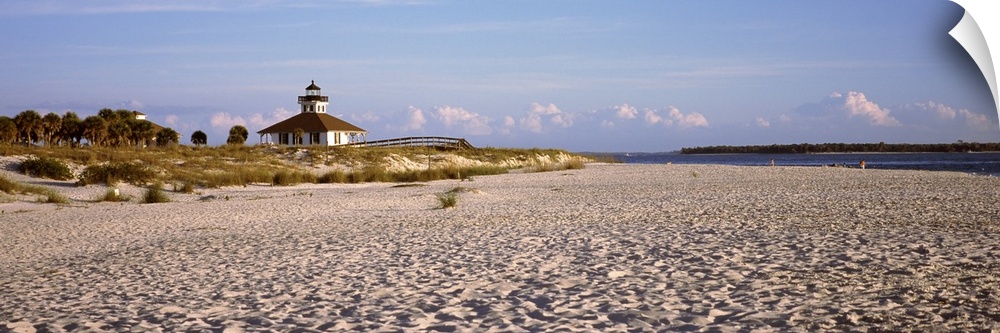 An elongated view of a beach with a lighthouse off in the distance on top of the dunes.