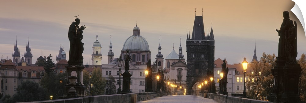 Wide angle photograph of the Charles Bridge at sunset.  Statues on either side of the bridge, the city skyline in the back...