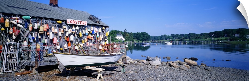 Panoramic photograph taken of a lobster shack with small buoys lining one side of it that sits on the edge of a body of wa...