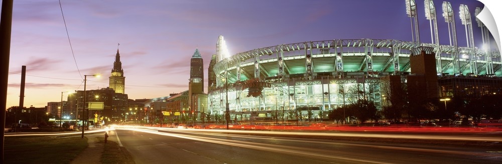 Panoramic photograph of sports arena light up at night with city skyline in the distance.