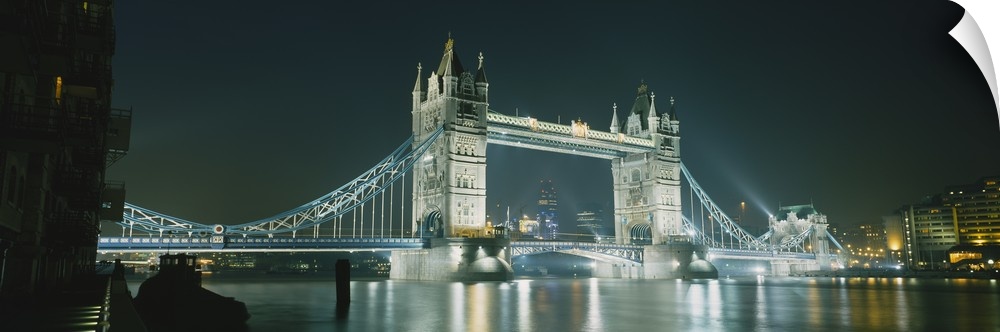 Panoramic photograph taken of the London tower bridge illuminated under a dark night sky.