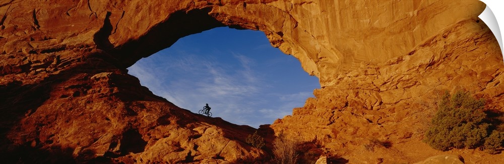 Giant, horizontal, wide angle photograph of the side of a mountain in Utah.  There is a mountain biker in an eye shaped op...
