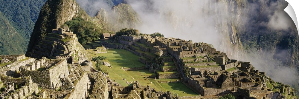 Oversized landscape photograph of Machu Picchu in the sunlight, thin clouds in the background, in Peru.