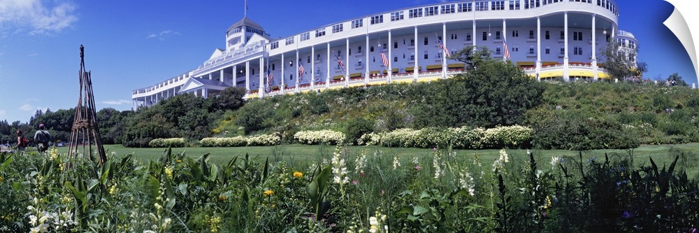 Panoramic photograph of huge building with columns with flower meadow in the foreground under a clear sky.