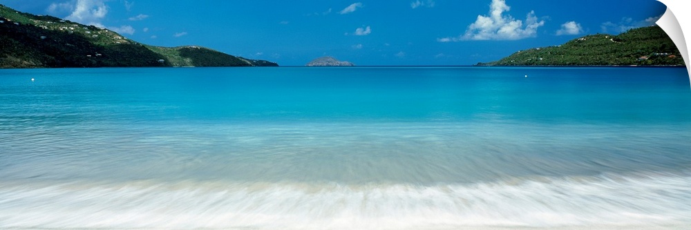 Panoramic photograph of clear water in a calm sea washing up a tropical beach.