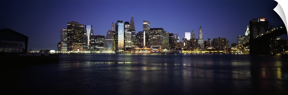 Panoramic photo of the NYC cityscape lit up at night seen from the water.