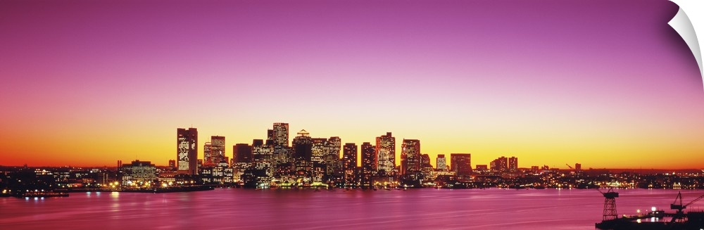 Big, wide angle photograph of a distant Boston skyline, with lit skyscrapers at sunset.