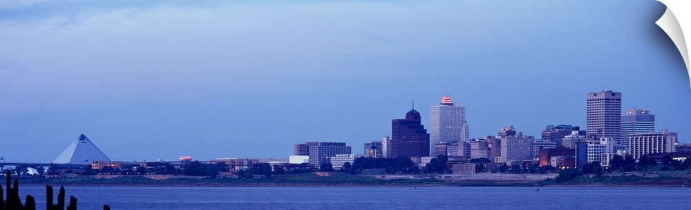 The skyline in Memphis Tennessee is photographed from a distance across a body of water. There is a cool tone over the ent...