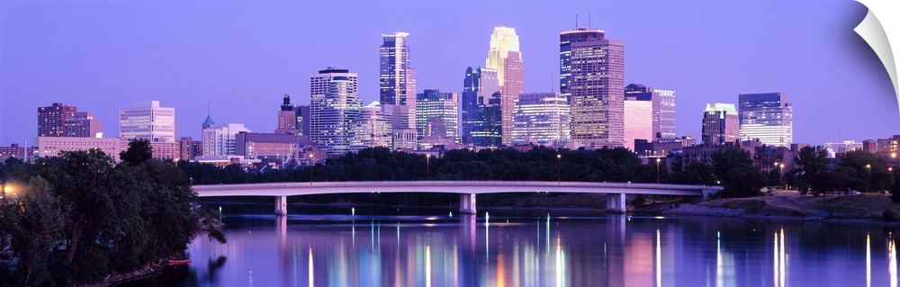 Panoramic photograph of cityscape with downtown building lit up.  The lights and building are reflected in water.