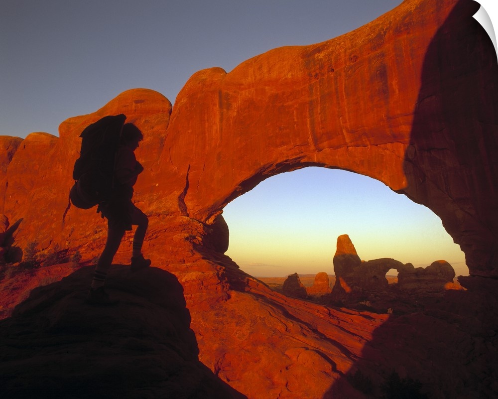 A hiker is photographed looking out onto massive cliffs and arches in a Utah national park.