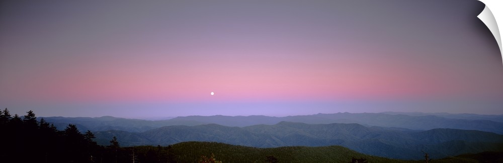 Mountains in the distance are photographed under a sunset sky with a small view of the moon.
