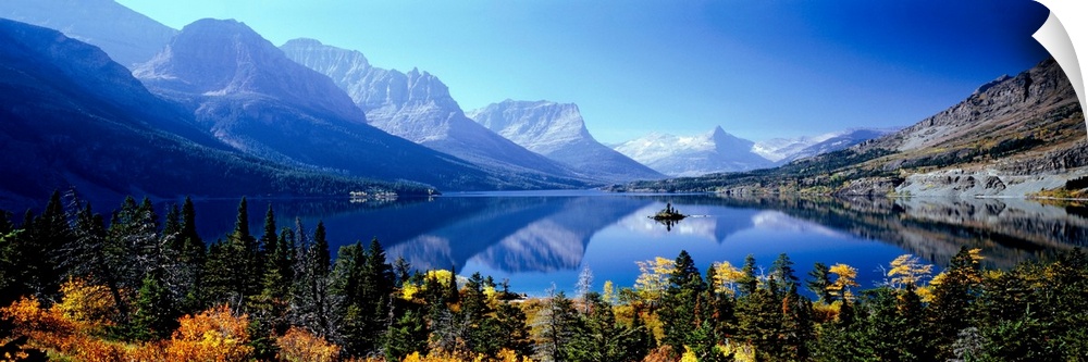 A panoramic photograph of mountains reflecting in a still lake surrounded by trees in this landscape of the wilderness.