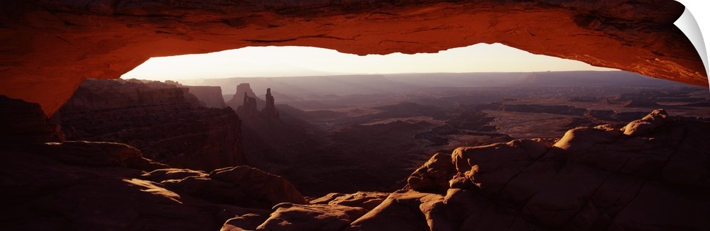 View through a stone arch in the morning, looking over the desert valley of eroded rock.